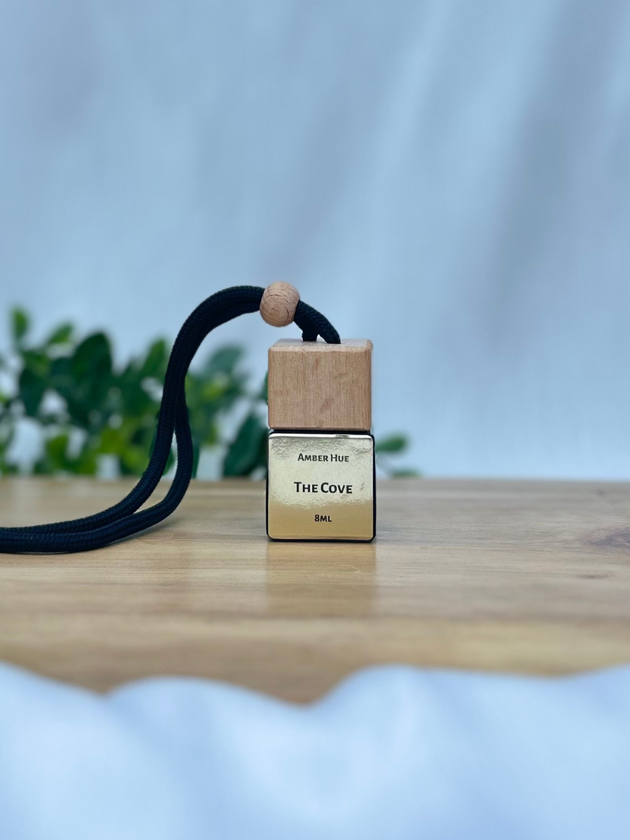 Small wooden and gold bottle with a black cord on a wooden surface with a blurred green plant background